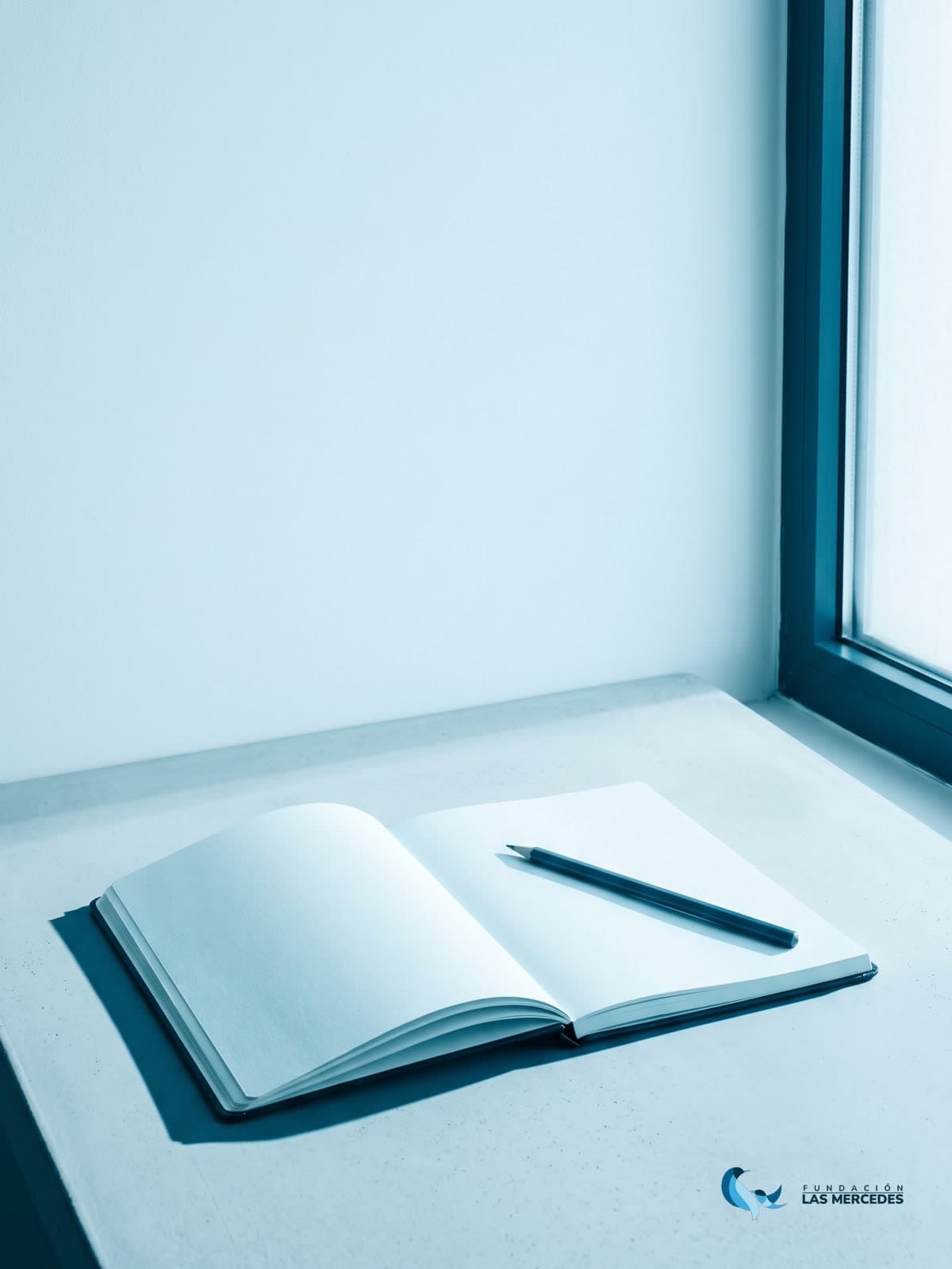 Un cuaderno abierto en blanco con un lápiz, junto a una ventana con luz de mañana