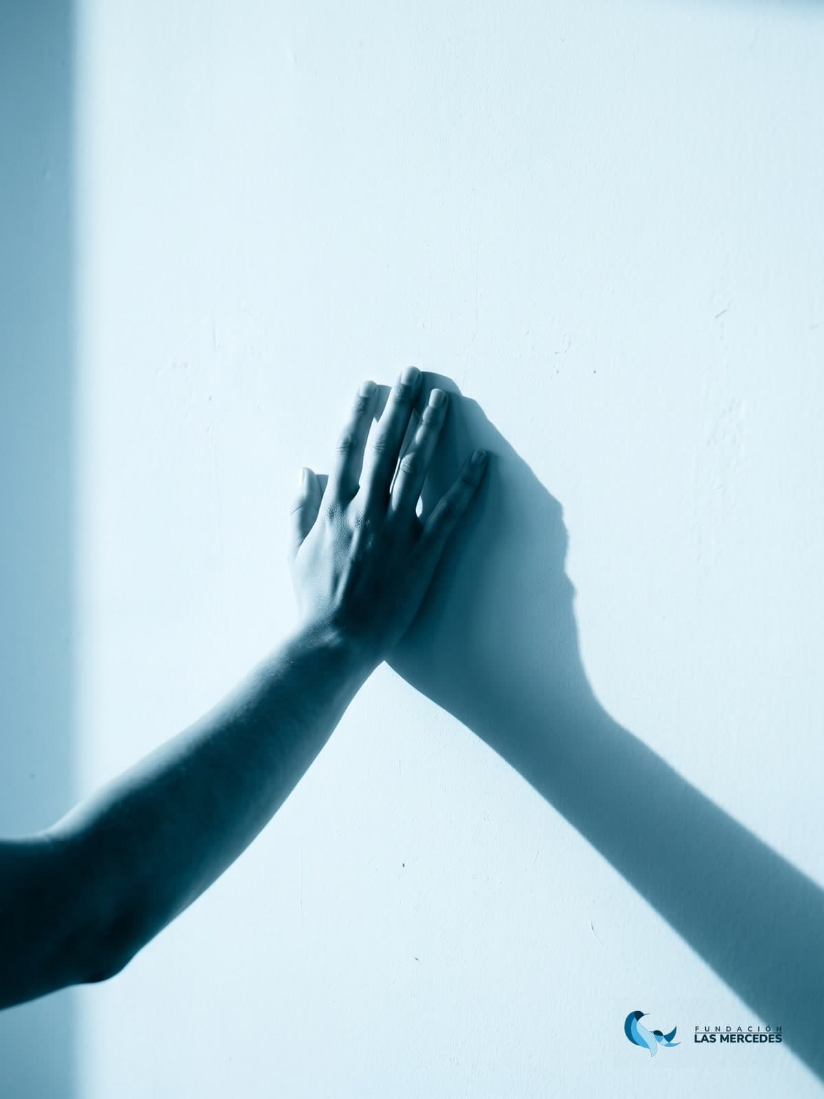 Una mano apoyada en un muro iluminado por luz suave, con su sombra proyectada
