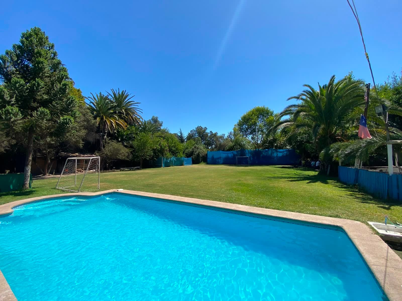 Piscina exterior en verano, con el césped y la bandera chilena al fondo