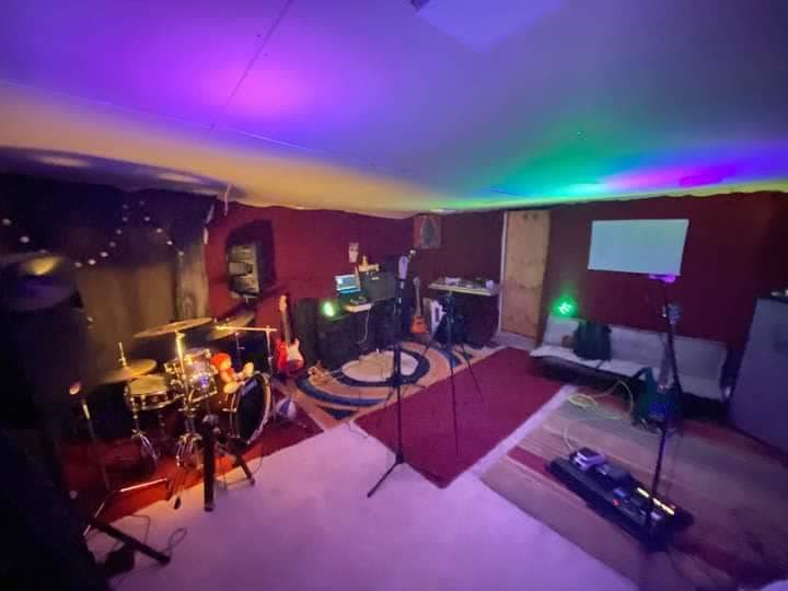 Sala de ensayo con batería, guitarras y luces de escenario